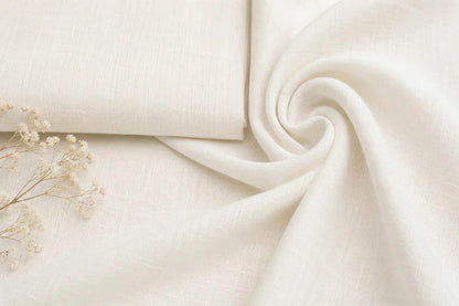 May include: A piece of off-white fabric with a visible woven texture, folded into a rectangular shape on one side and draped into a soft, swirling spiral on the other, accompanied by a small sprig of dried white baby's breath flowers.
