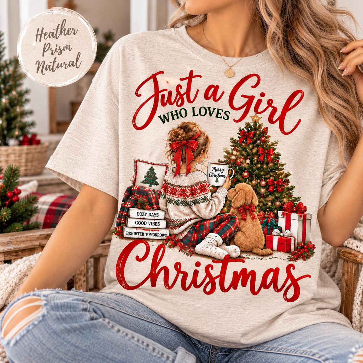 May include: A heather natural t-shirt featuring a graphic of a person with a red hair bow sitting by a decorated Christmas tree with a dog. The text reads Just a Girl Who Loves Christmas, Merry Christmas, Cozy Days, Good Vibes, Brighter Tomorrows.