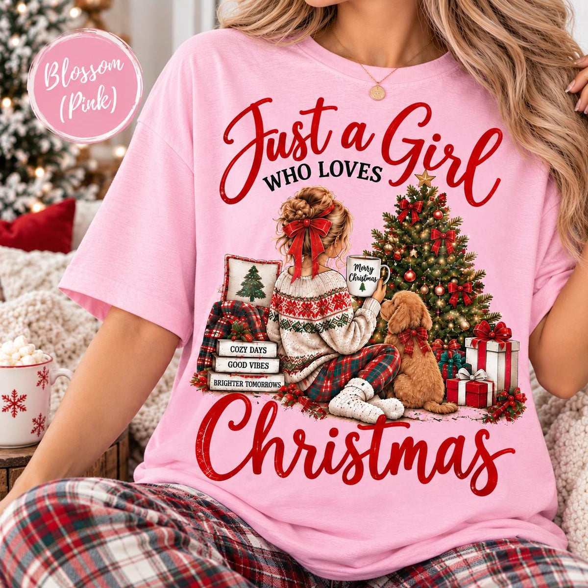 May include: A light pink t-shirt featuring a graphic of a person with a red hair bow sitting by a Christmas tree with a dog. The text reads Just a Girl WHO LOVES CHRISTMAS, Merry Christmas, COZY DAYS, GOOD VIBES, and BRIGHTER TOMORROWS.
