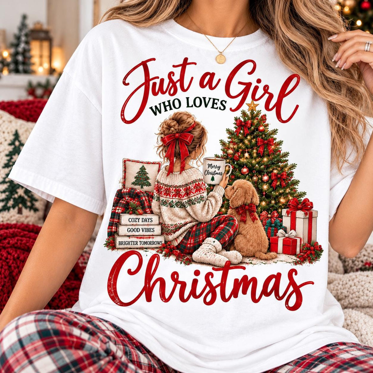 May include: A white t-shirt featuring a graphic of a person with a red hair bow sitting by a Christmas tree with a dog. The text reads "Just a Girl WHO LOVES CHRISTMAS" with "COZY DAYS", "GOOD VIBES", and "BRIGHTER TOMORROWS" on stacked books.
