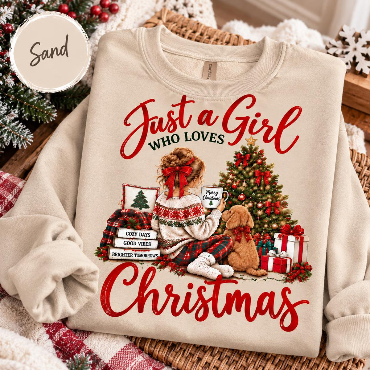 May include: A sand-colored crewneck sweatshirt featuring a graphic of a person with a red hair bow sitting by a Christmas tree with a dog. The text reads Just a Girl WHO LOVES CHRISTMAS, with stacked books labeled COZY DAYS, GOOD VIBES, BRIGHTER TOMORROWS.