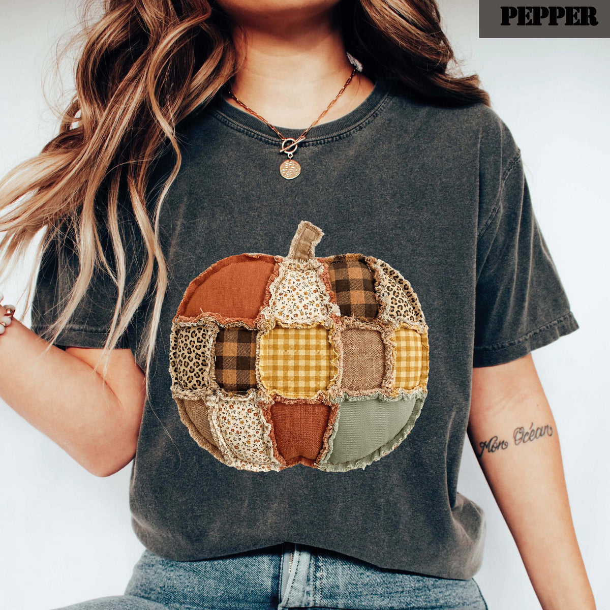 May include: A charcoal gray t-shirt featuring a large, central pumpkin graphic composed of various fabric patches in shades of orange, brown, yellow, and green, with leopard print and plaid patterns. The text PEPPER appears in the top corner.