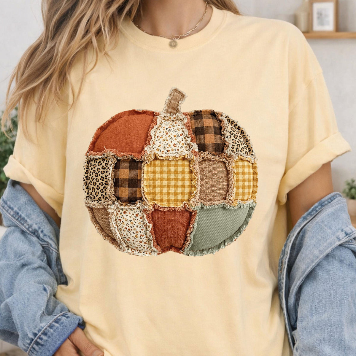 May include: A pale yellow short-sleeve t-shirt featuring a large central graphic of a pumpkin constructed from various fabric patches. The pumpkin design includes patterns such as leopard print, brown plaid, yellow gingham, and floral prints.