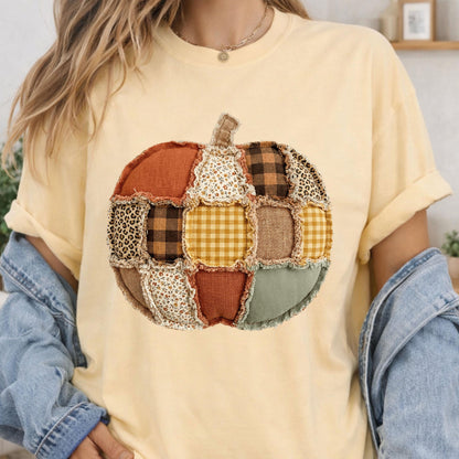 May include: A pale yellow short-sleeve t-shirt featuring a large central graphic of a pumpkin constructed from various fabric patches. The pumpkin design includes patterns such as leopard print, brown plaid, yellow gingham, and floral prints.