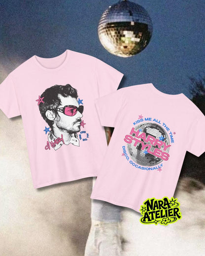 May include: A light pink t-shirt featuring a graphic of a person wearing pink-tinted sunglasses on the front and a disco ball graphic with the text "KISS ME ALL THE TIME HARRY STYLES DISCO OCCASIONALLY" on the back, accented with small blue and pink stars.