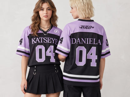 May include: A black and lavender mesh jersey featuring the text KATSEYE and the number 04 on the front, and the text WILD, DANIELA, and the number 04 on the back. The jersey has short sleeves with white and black stripes and a V-neck collar.