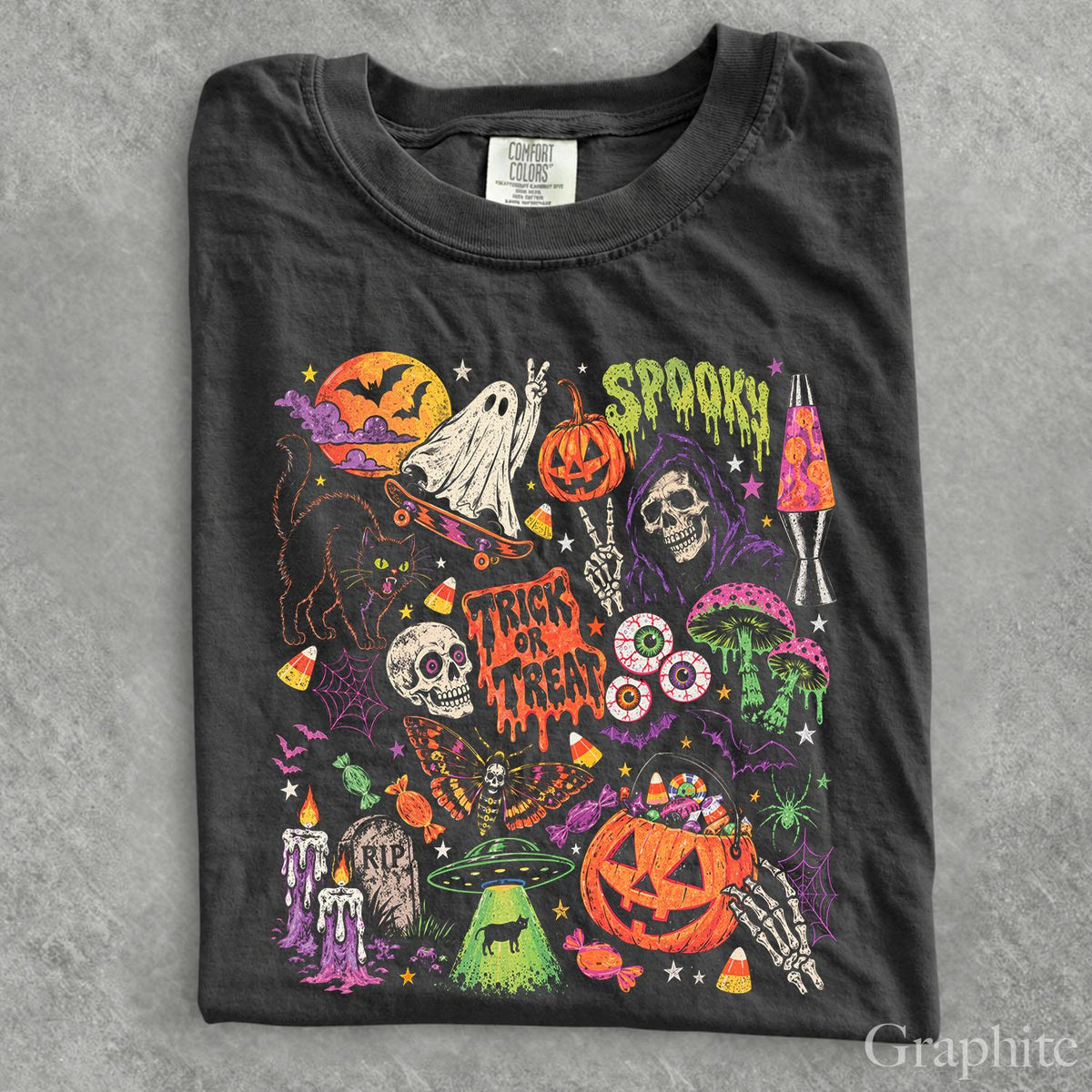 May include: A charcoal gray t-shirt featuring a vibrant Halloween-themed graphic print. The design includes a ghost on a skateboard, a black cat, a skull, a pumpkin, a moth, a tombstone, a lava lamp, and the text Trick or Treat and Spooky.