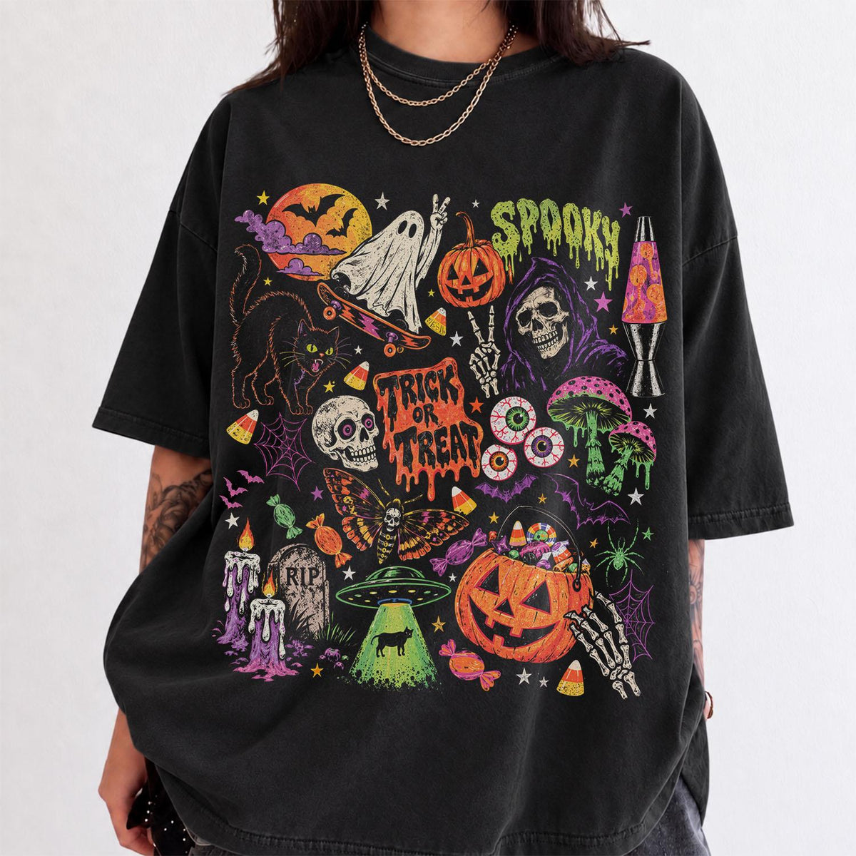 May include: A black short-sleeve t-shirt featuring a colorful graphic print of Halloween-themed imagery including a ghost on a skateboard, a pumpkin, a skull, a lava lamp, a moth, a UFO, and the text "SPOOKY" and "TRICK OR TREAT" in a dripping font.