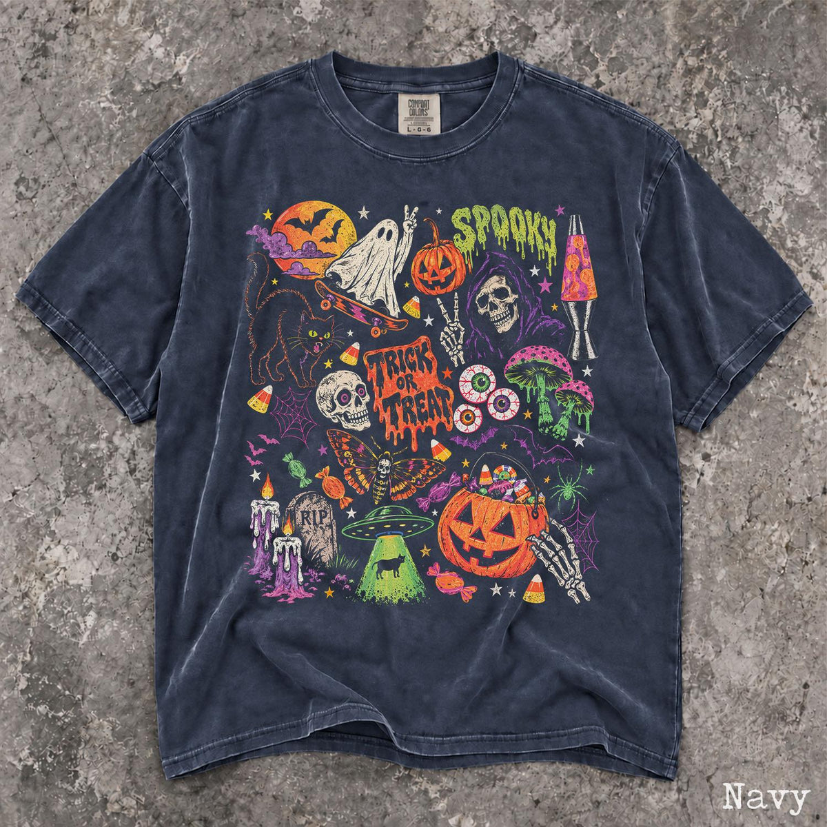 May include: A navy blue t-shirt featuring a vibrant Halloween-themed graphic print. The design includes a ghost on a skateboard, a jack-o'-lantern, a skull, a black cat, a UFO, mushrooms, and the text "SPOOKY" and "TRICK OR TREAT" in colorful ink.