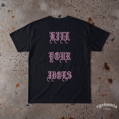 May include: A black short-sleeved t-shirt featuring the text "KILL YOUR IDOLS" printed in a light pink gothic-style font across the center. The garment has a crew neckline and a standard fit, displaying the back side of the shirt.