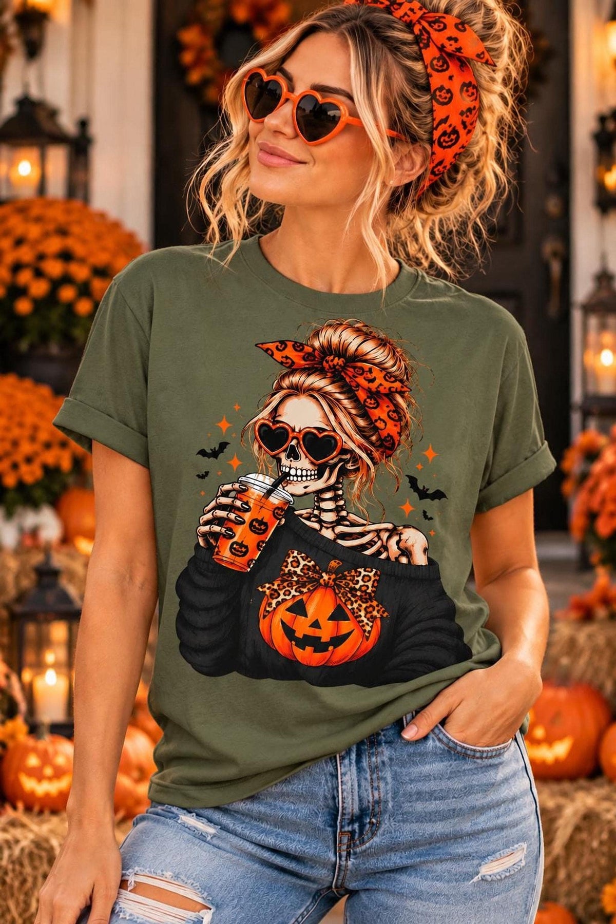 A woman wearing a military green t-shirt with a skeleton graphic holding a pumpkin cup and wearing heart-shaped sunglasses.