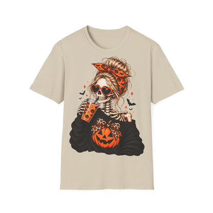 A beige t-shirt centered with a graphic of a skeleton woman with a bun and orange patterned headband wearing heart-shaped sunglasses and drinking from a cup.