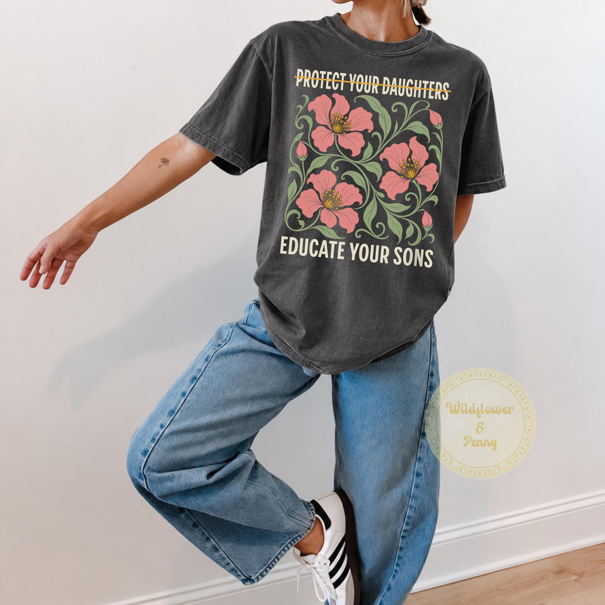 May include: A charcoal gray short-sleeve t-shirt featuring a graphic print of pink flowers with green leaves. The text reads PROTECT YOUR DAUGHTERS with a line through it and EDUCATE YOUR SONS below the floral design in a cream-colored font.