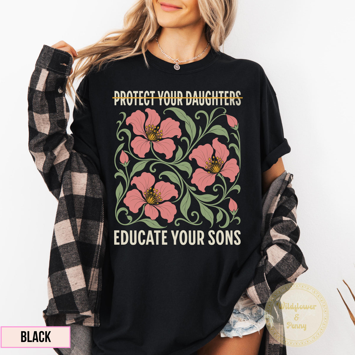 May include: A black t-shirt featuring a graphic print with the text PROTECT YOUR DAUGHTERS at the top and EDUCATE YOUR SONS at the bottom. The center design displays pink flowers with green leaves and swirling vines on a dark background.