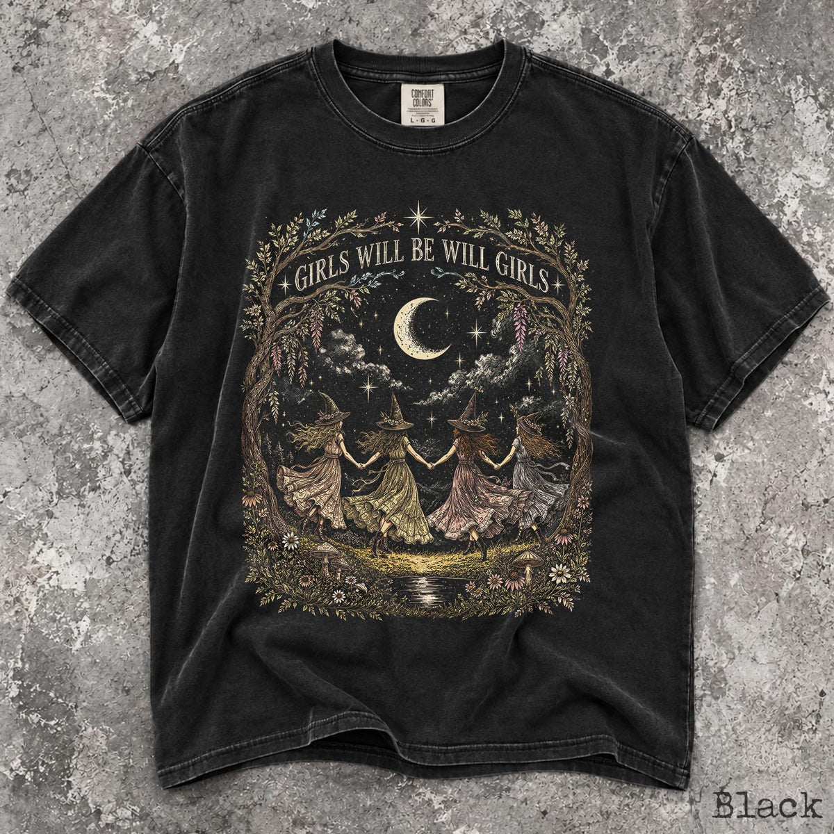 May include: A black short-sleeve t-shirt featuring a graphic print of four figures in pointed hats holding hands in a circle under a crescent moon. The text "GIRLS WILL BE WILL GIRLS" is arched above the figures, surrounded by trees and flowers.