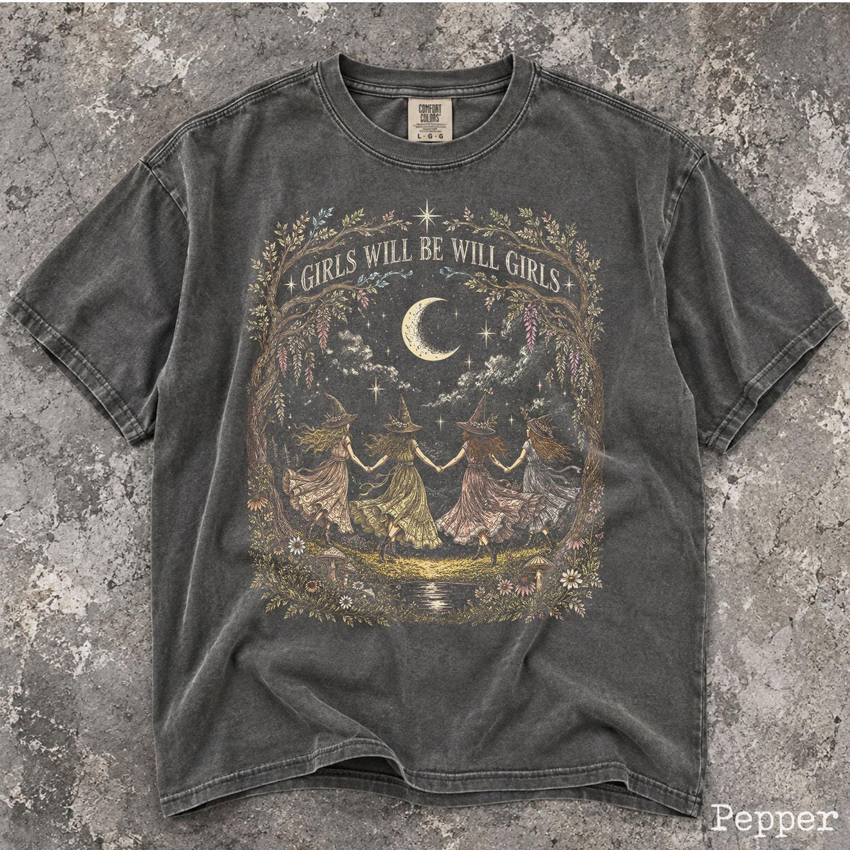 May include: A charcoal gray short-sleeve t-shirt featuring a graphic print of four figures in pointed hats holding hands under a crescent moon. The text "GIRLS WILL BE WILL GIRLS" is arched above the figures, surrounded by a detailed floral border.