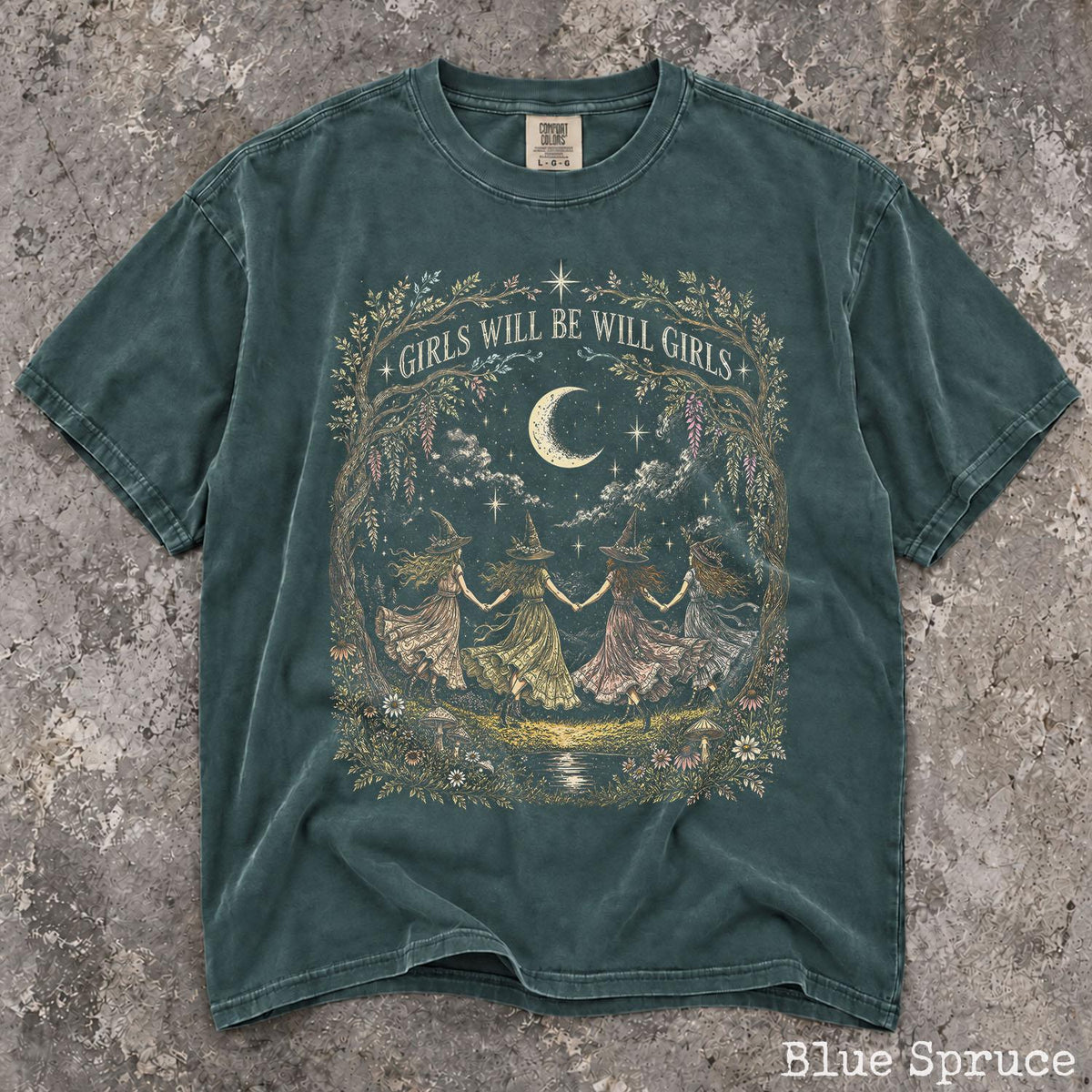 May include: A blue spruce short-sleeve t-shirt featuring a graphic print of four figures in witch hats holding hands in a circle under a crescent moon. The text GIRLS WILL BE WILL GIRLS is printed above the figures, surrounded by a floral frame.