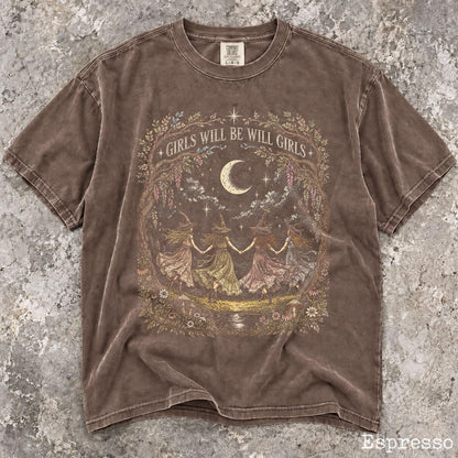 May include: A brown short-sleeve t-shirt featuring a graphic print of four figures in hats holding hands in a circle under a crescent moon. The text GIRLS WILL BE WILL GIRLS is printed above the moon. The design is framed by a floral wreath.