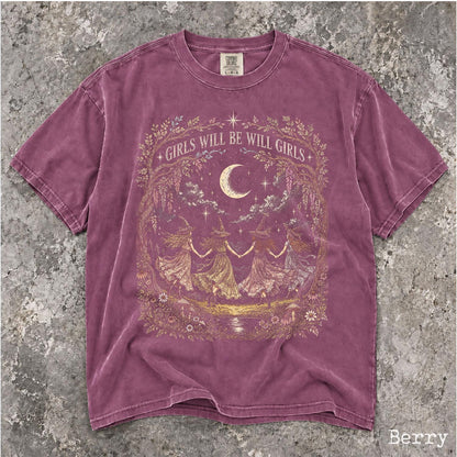 May include: A berry-colored short-sleeve t-shirt featuring a gold graphic print of four figures in pointed hats holding hands in a circle under a crescent moon. The text GIRLS WILL BE WILL GIRLS is printed in an arch above the central illustration.