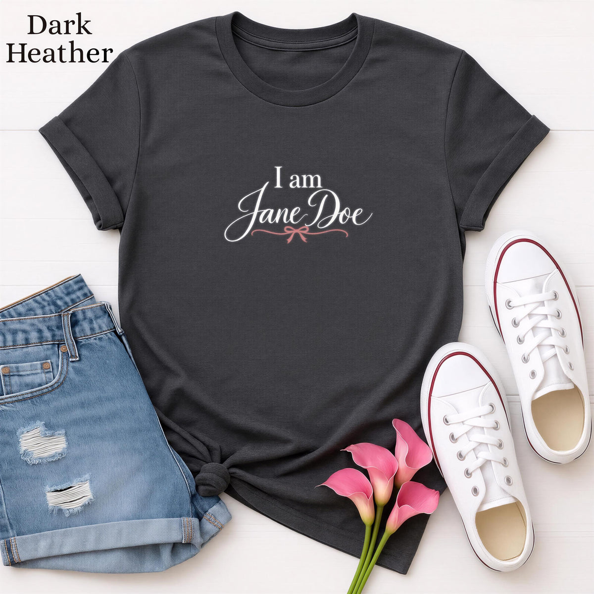 a casual outfit consisting of a black t-shirt with the text "I am Jane Doe" printed on it, a pair of blue jeans, and white sneakers. The outfit is laid out on a white background, with a bouquet of pink flowers placed next to the jeans and sneakers.