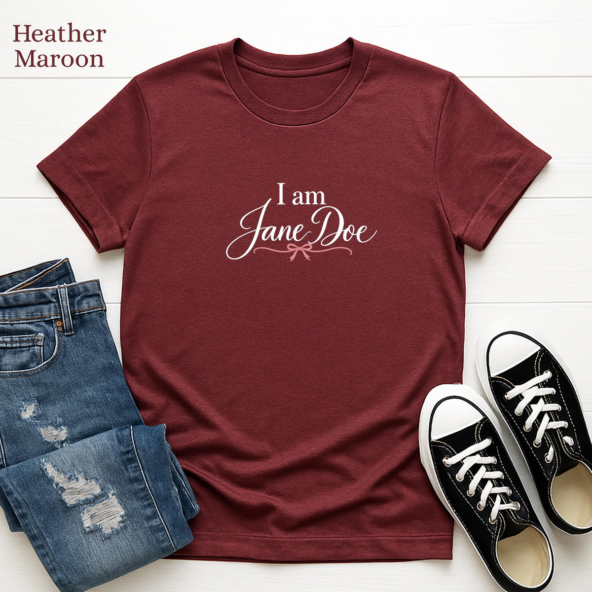 A burgundy t-shirt with the text "I am Jane Doe" printed on it, along with a pair of blue jeans and black and white sneakers.