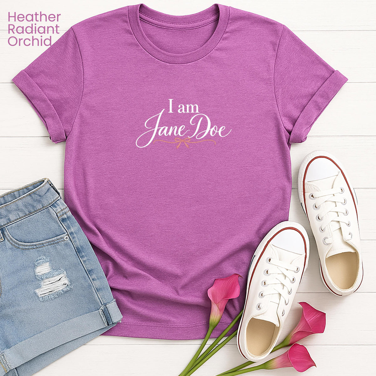 a purple t-shirt with the text "I am Jane Doe" printed on it, along with a pair of denim shorts and white sneakers. There are also pink flowers in the foreground.