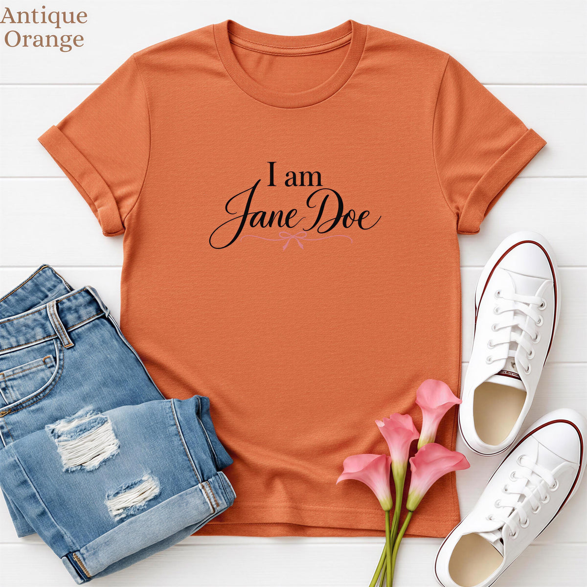 a casual outfit consisting of a red t-shirt with the text "I am Jane Doe", a pair of blue jeans, white sneakers, and pink flowers.