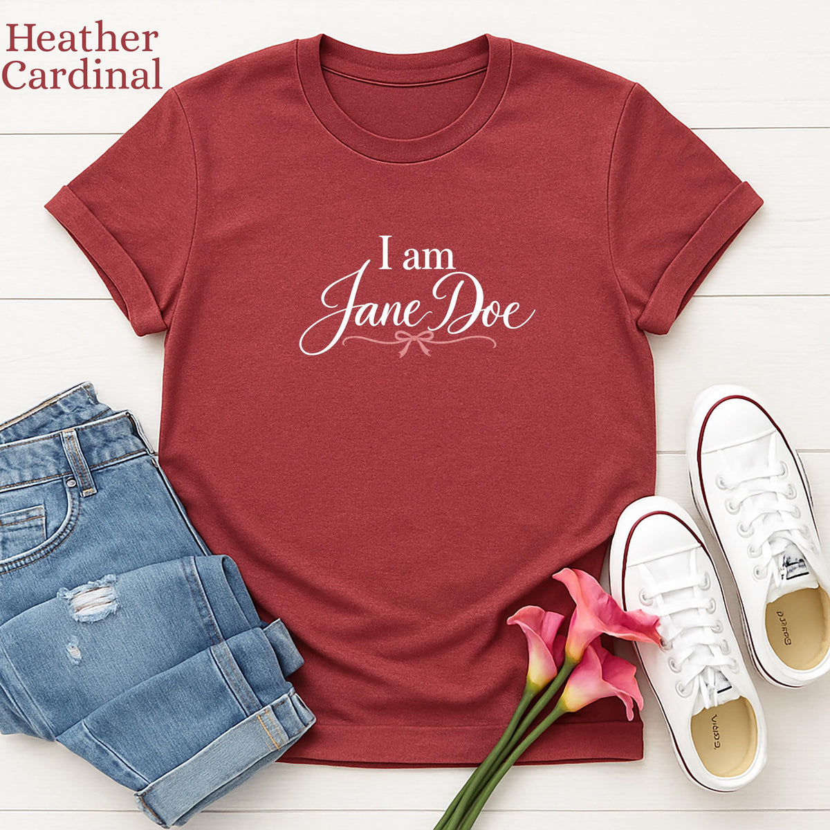 a red t-shirt with the text "I am Jane Doe" printed on it, along with a pair of blue jeans and white sneakers. There are also pink flowers arranged on the side.