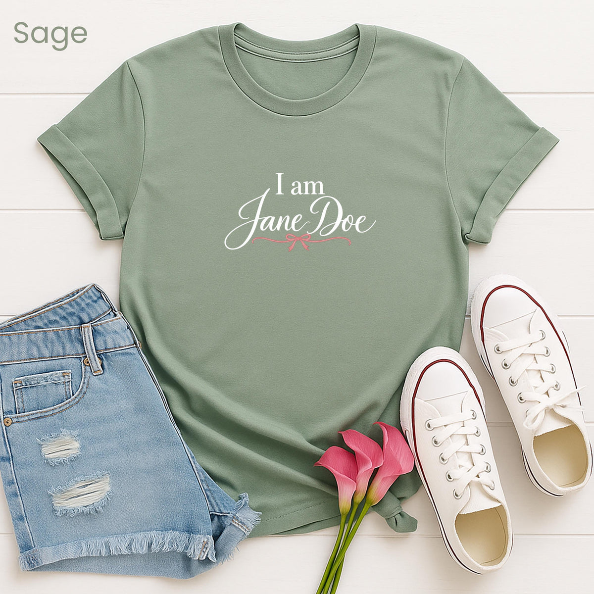 A green t-shirt with the text "I am Jane Doe" printed on it, along with a pair of denim shorts and white sneakers, all laid out on a white background.