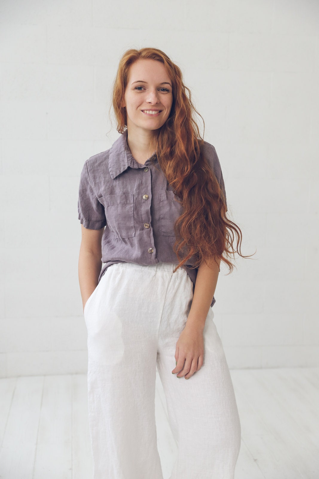 May include: A woman wearing a purple linen shirt with a white linen button-down collar and white linen pants.