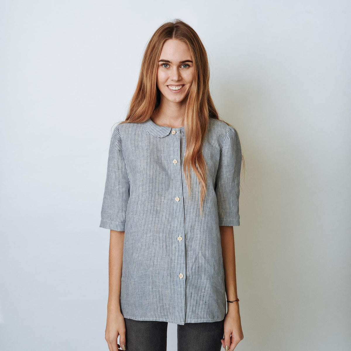 May include: A woman wearing a blue and white striped collared shirt with a peter pan collar. She is smiling and looking at the camera.