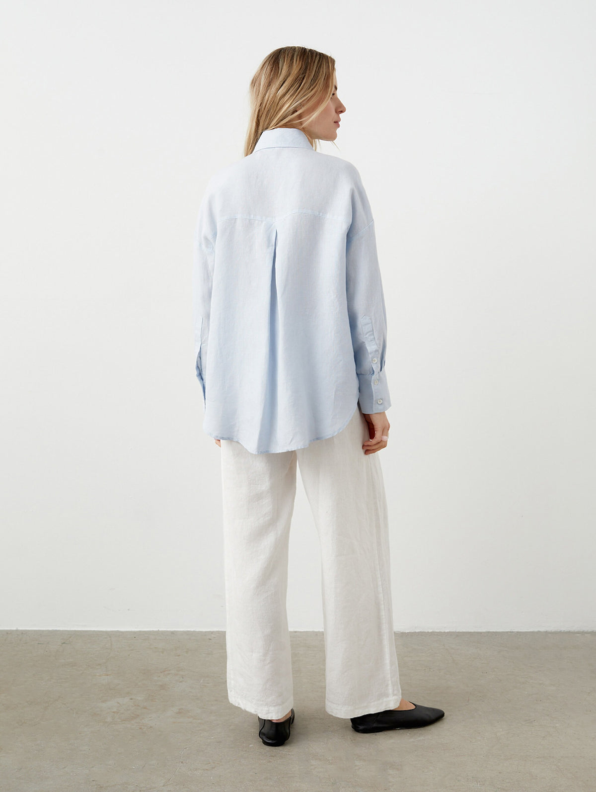 May include: A light blue button-down shirt and white linen pants. The shirt has long sleeves and a classic collar. The pants are wide-legged. The outfit is completed with black flats. The clothing is made of a lightweight fabric.