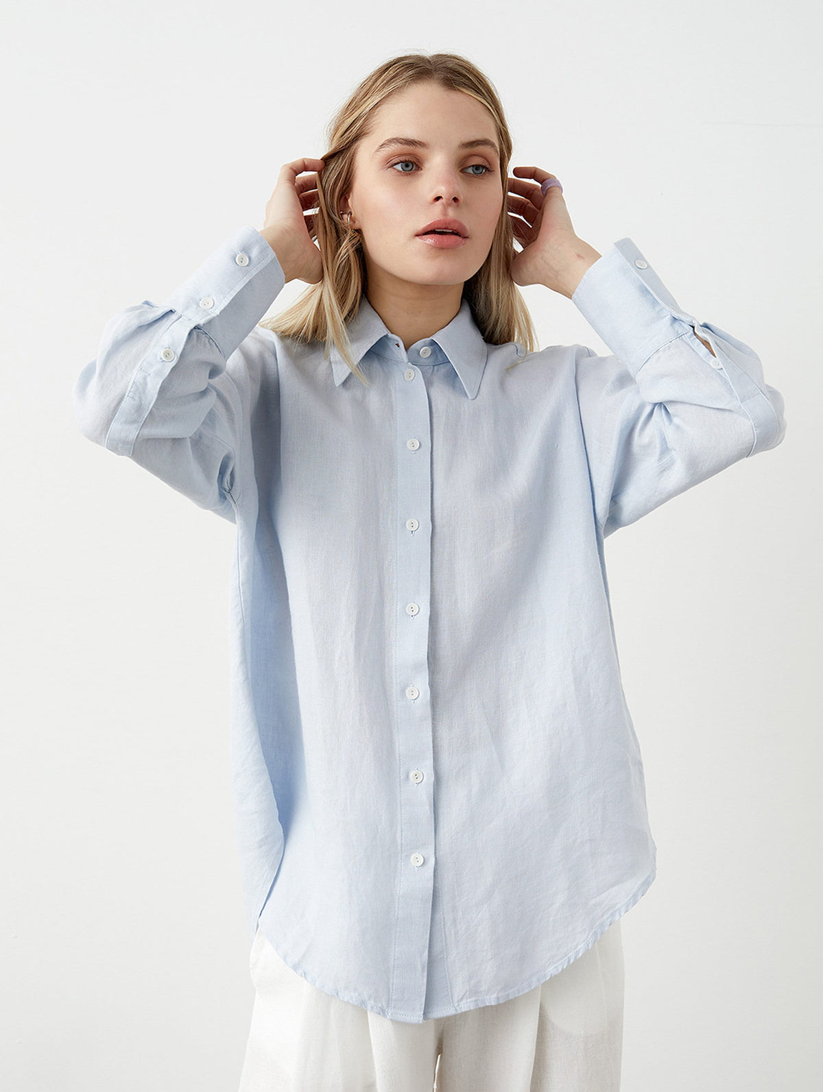 May include: A light blue button-down shirt with long sleeves and a classic collar. The shirt has buttoned cuffs and a curved hem. The fabric appears to be a lightweight linen or cotton blend. The shirt is unbuttoned at the top.