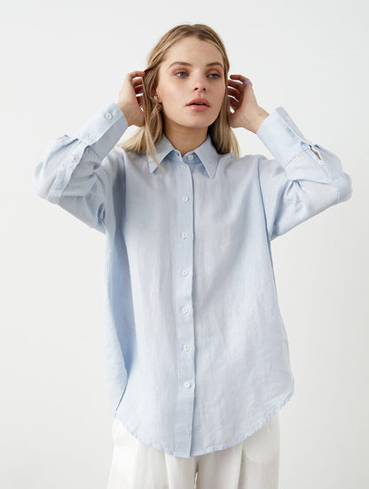 May include: A light blue button-down shirt with long sleeves and a classic collar. The shirt has buttoned cuffs and a curved hem. The fabric appears to be a lightweight linen or cotton blend. The shirt is unbuttoned at the top.