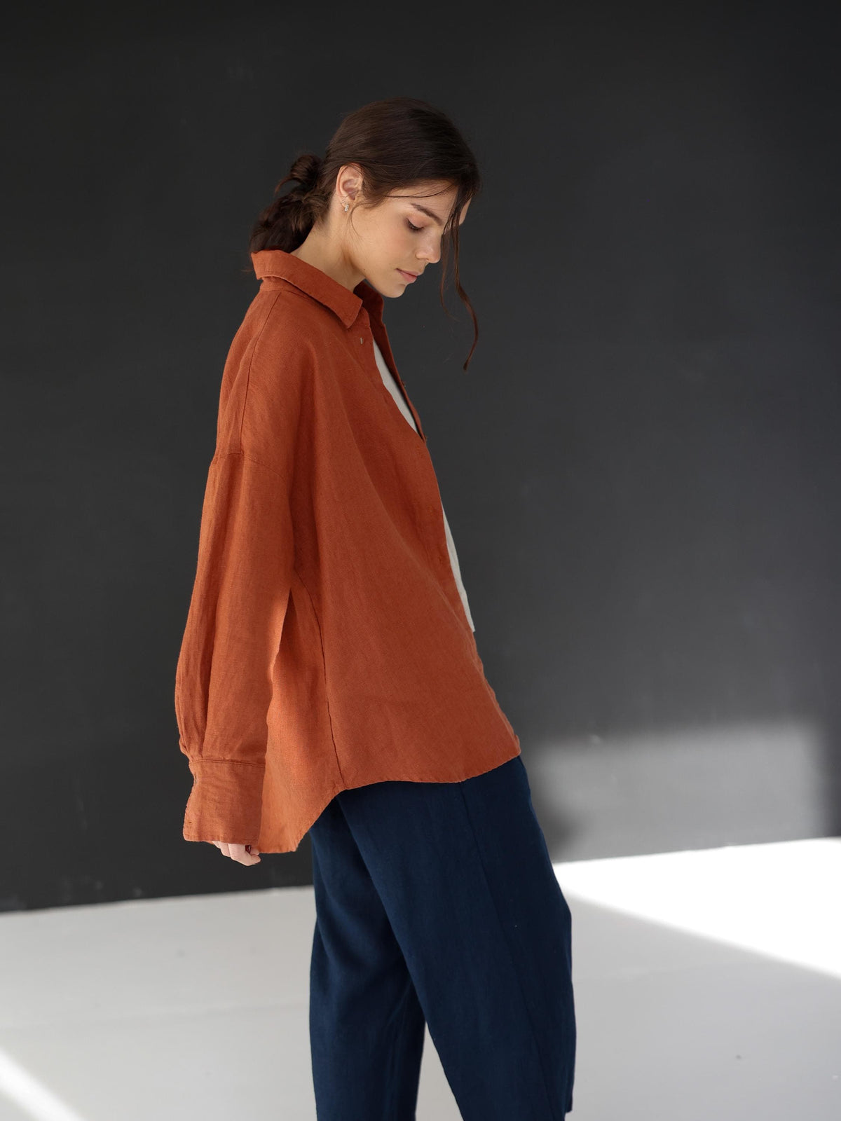 May include: A rust-colored linen shirt with long sleeves and a collared neckline. The shirt is paired with navy blue pants. The outfit is simple and elegant, suitable for casual wear.